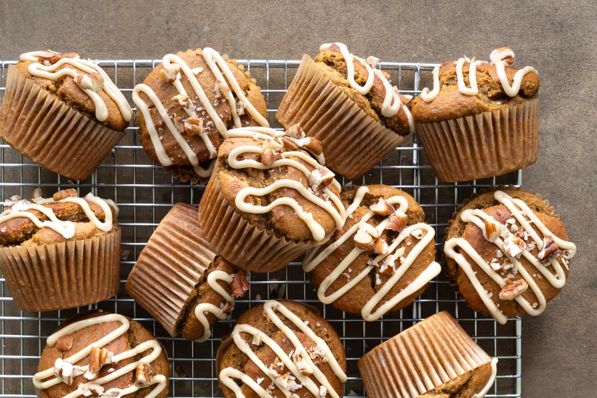 Pumpkin muffins with maple glaze and pecans on a cooling rack with one muffin stacked on top