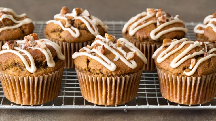 Pumpkin oatmeal muffins lined up on a cooling rack and topped with maple glaze and chopped pecans